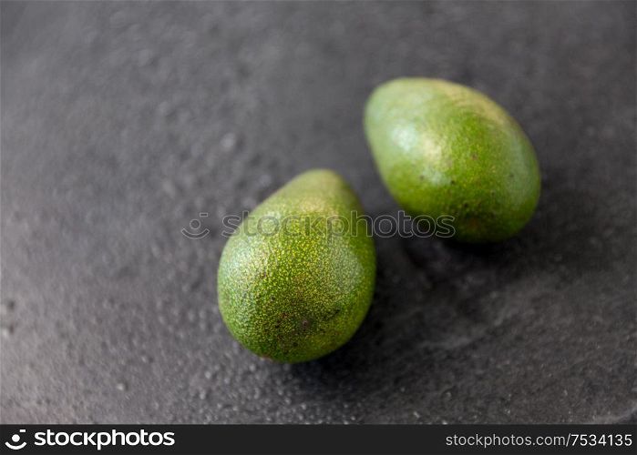 food, eating and vegetable concept - close up of two avocados on wet slate stone background. two avocados on wet slate stone background