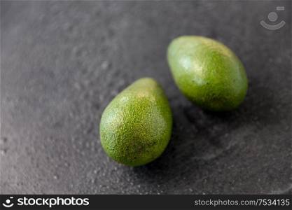 food, eating and vegetable concept - close up of two avocados on wet slate stone background. two avocados on wet slate stone background