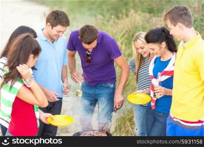 food, eating, cooking, summer holidays and people concept - group of friends having picnic and making barbecue on beach