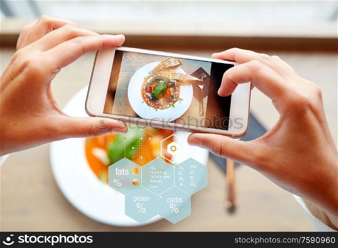 food, eating, technology, culinary and people concept - close up of hands with gazpacho soup on smartphone screen and nutritional value chart at restaurant. hands with phone and food nutritional value chart