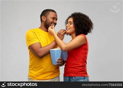 food, entertainment and people concept - happy smiling african american couple eating popcorn over grey background. happy african american couple eating popcorn