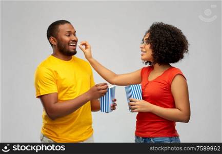 food, entertainment and people concept - happy smiling african american couple eating popcorn over grey background. happy african american couple eating popcorn