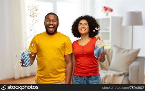 food, entertainment and people concept - happy smiling african american couple with popcorn flying in air over home background. happy african american couple with popcorn