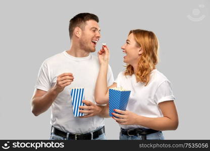 food, entertainment and people concept - portrait of happy couple in white t-shirts eating popcorn over grey background. happy couple in white t-shirts eating popcorn