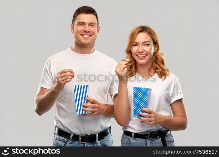 food, entertainment and people concept - portrait of happy couple in white t-shirts eating popcorn over grey background. happy couple in white t-shirts eating popcorn