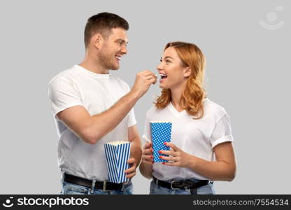 food, entertainment and people concept - portrait of happy couple in white t-shirts eating popcorn over grey background. happy couple in white t-shirts eating popcorn