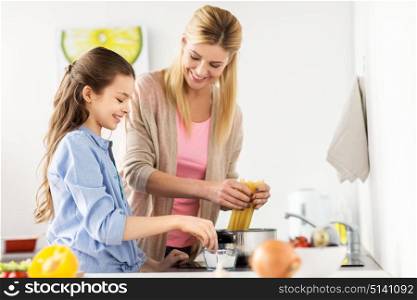 food, family and people concept - happy mother and daughter cooking and boiling spaghetti pasta for dinner at home kitchen. happy family cooking food at home kitchen