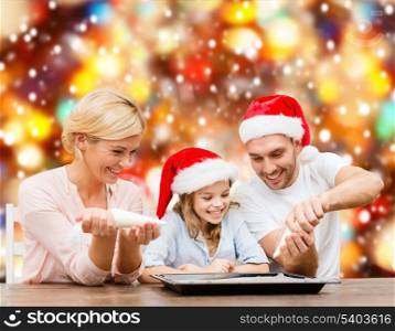 food, family, christmas, hapiness and people concept - smiling family in santa helper hats decorating cookies with glaze