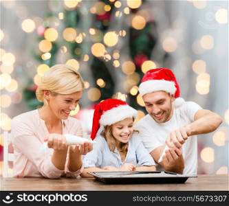food, family, happiness and people concept - smiling family in santa helper hats with glaze and pan cooking over christmas tree lights background