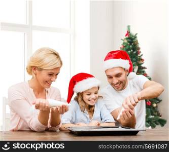 food, family, happiness and people concept - smiling family in santa helper hats with glaze and pan cooking over living room and christmas tree background