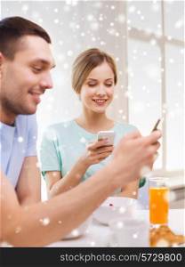 food, family, people and technology concept - smiling couple with smartphones and having breakfast at home