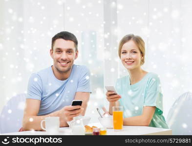 food, family, people and technology concept - smiling couple with smartphones and having breakfast at home