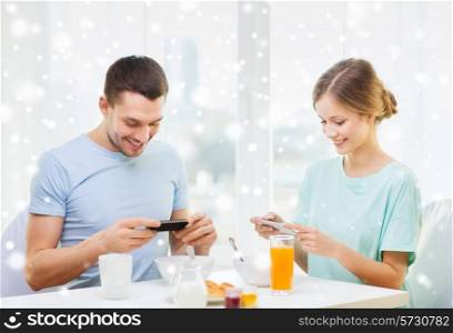 food, family, people and technology concept - smiling couple with smartphones and having breakfast at home