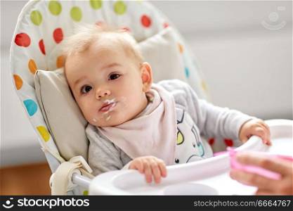 food, feeding and childhood concept - little baby girl eating in highchair at home. little baby girl eating in highchair at home