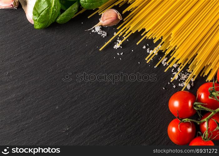 Food frame photo. Pasta ingredients. Cherry-tomatoes, spaghetti pasta, garlic, basil, salt on dark grunge backdrop, copy space, top view, horizontal