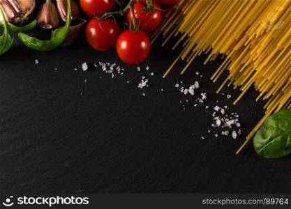 Food frame photo. Pasta ingredients. Cherry-tomatoes, spaghetti pasta, garlic, basil, salt on dark grunge backdrop, copy space, top view, horizontal