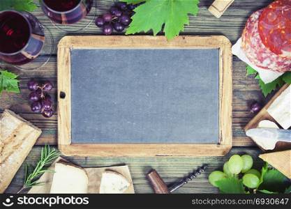 Food frame. Wine and snack set with red wine in glasses, meat variety, bread, cheese and grape on rustic wooden background, top view, copy space in center