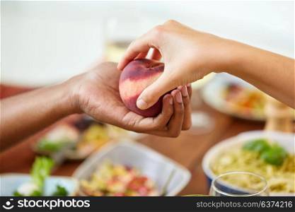 food, fruit and healthy eating concept - multiracial couple hands with peach. multiracial couple hands with peach