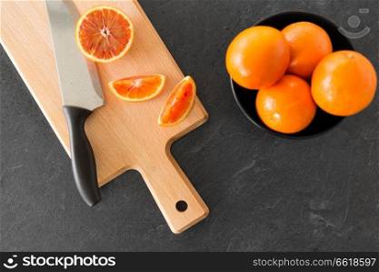 food, fruits and healthy eating concept - close up of blood oranges and kitchen knife on wooden cutting board. close up of oranges and knife on cutting board