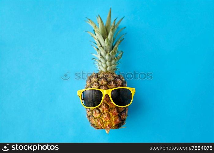 food, fruits and healthy eating concept - close up of pineapple in yellow sunglasses on blue background. pineapple in yellow sunglasses on blue background