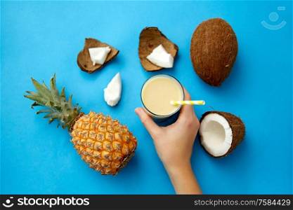 food, fruits and healthy eating concept - hand with pineapple coconut drink in glass with paper straw on blue background. hand with pineapple coconut drink with paper straw