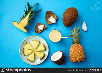 food, fruits and healthy eating concept - pineapple, coconut and glass of drink with paper straw on blue background. pineapple, coconut and drink with paper straw
