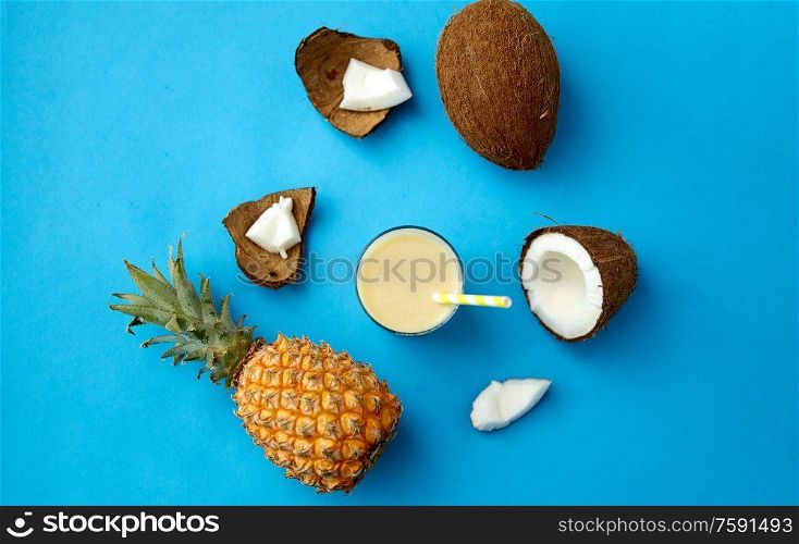 food, fruits and healthy eating concept - pineapple, coconut and glass of drink with paper straw on blue background. pineapple, coconut and drink with paper straw