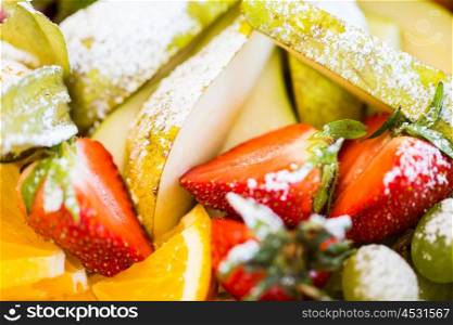 food, fruits, dessert and summer concept - close up of dish with sugared strawberries, pears and orange