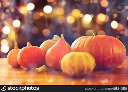 food, halloween, harvest, season and autumn concept - close up of pumpkins on wooden table over holidays lights