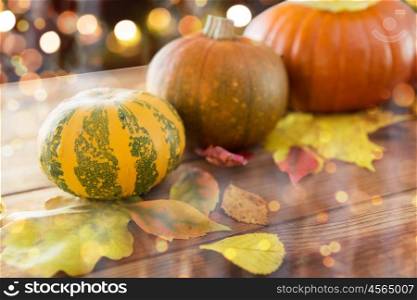 food, halloween, harvest, season and autumn concept - close up of pumpkins and leaves on wooden table over holidays lights
