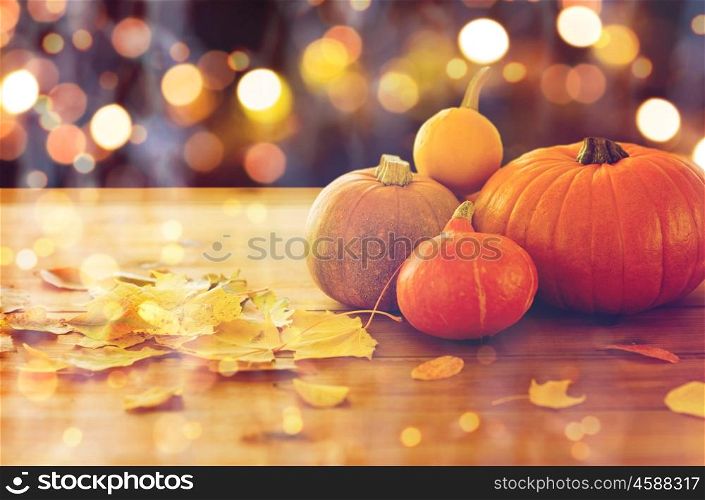food, halloween, harvest, season and autumn concept - close up of pumpkins and leaves on wooden table over holidays lights. close up of halloween pumpkins on wooden table