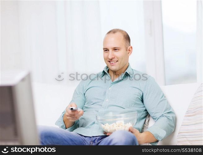 food, happiness and people concept - smiling man with popcorn watching movie at home