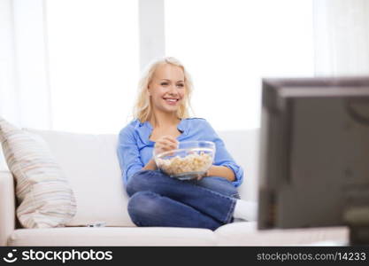 food, happiness and people concept - smiling young girl with popcorn watching movie at home