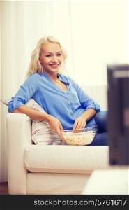 food, happiness and people concept - smiling young girl with popcorn watching movie at home