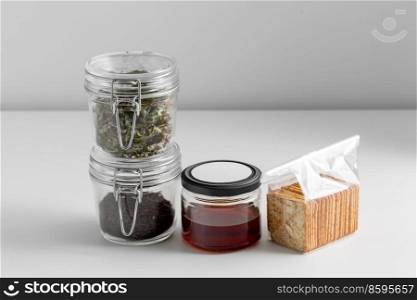 food, hea<hy eating and diet concept - jars with dried herbs, tea, ho≠y and cookies on white background. jars with dried herb, tea, ho≠y and cookies