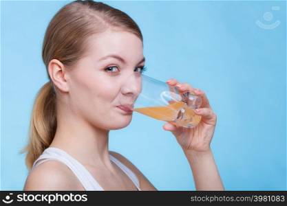 Food, health concept. Woman holding glass of orange flavored drink and drinking from it. Studio shot on blue background. Woman drinking orange flavored drink or juice