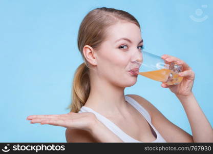 Food, health concept. Woman holding glass of orange flavored drink and drinking from it. Studio shot on blue background. Woman drinking orange flavored drink or juice