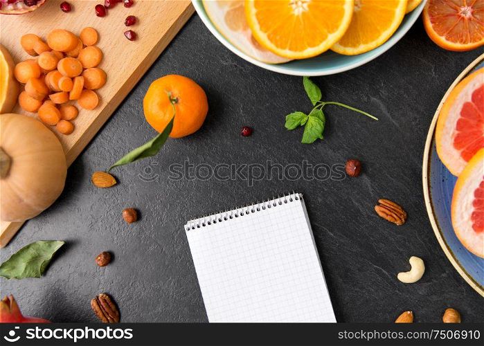 food, healthy eating and diet concept - close up of notebook, fruits and vegetables on slate table top. close up of notebook, fruits and vegetables