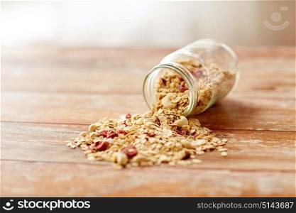 food, healthy eating and diet concept - jar with granola or muesli poured on wooden table. jar with granola or muesli poured on table