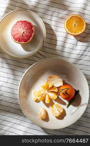 food, healthy eating and fruits concept - close up of mandarin, grapefruit and orange on plates over drapery. still life with mandarins and grapefruit on plate