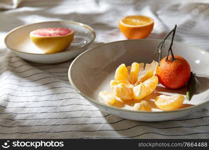 food, healthy eating and fruits concept - close up of mandarin, grapefruit and orange on plates over drapery. still life with mandarins and grapefruit on plate
