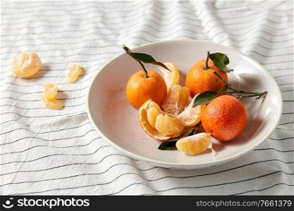 food, healthy eating and fruits concept - close up of mandarins on plate over drapery. still life with mandarins on plate over drapery