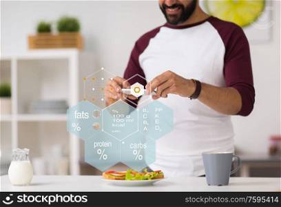 food, healthy eating and people concept - close up of man with smartphone having sandwiches for breakfast at home kitchen over nutritional value chart. man with phone and food nutritional value chart