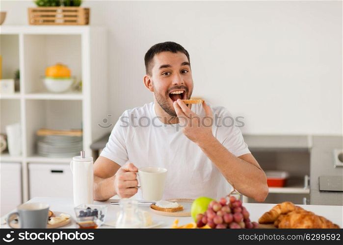 food, healthy eating and people concept - man having toast with coffee for breakfast at home kitchen. man eating toast with coffee at home kitchen
