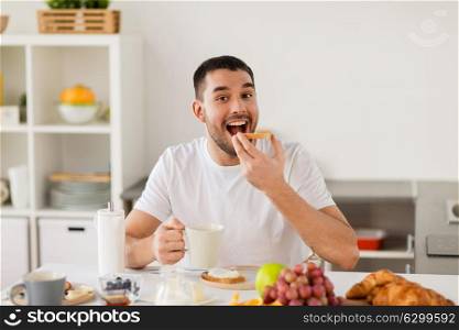 food, healthy eating and people concept - man having toast with coffee for breakfast at home kitchen. man eating toast with coffee at home kitchen