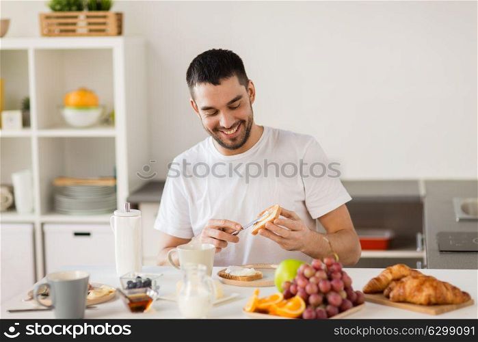 food, healthy eating and people concept - man making toast with cheese spread for breakfast at home kitchen. man eating toast with coffee at home kitchen