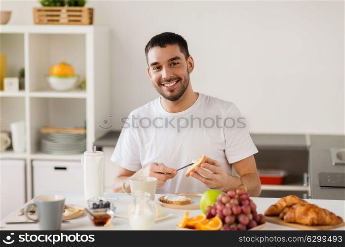 food, healthy eating and people concept - man making toast with cheese spread for breakfast at home kitchen. man eating toast with coffee at home kitchen