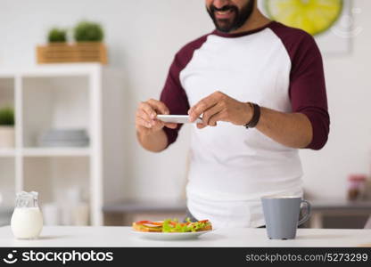 food, healthy eating and people concept - man with smartphone having breakfast and photographing sandwiches at home kitchen. man photographing food by smartphone at home