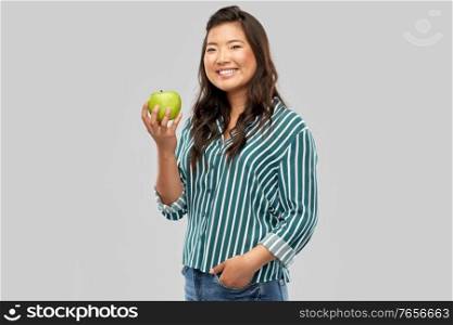 food, healthy eating and people concept - portrait of happy smiling asian woman holding green apple over grey background. happy smiling asian woman holding green apple