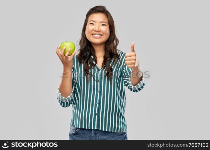 food, healthy eating and people concept - portrait of happy smiling asian woman holding green apple over grey background. happy smiling asian woman holding green apple